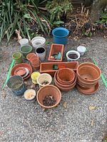Overview of assorted plant pots including terracotta, glazed, and plastic in various sizes and colors arranged on ground outdoors.