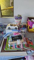 Overview of lot including Pottery Barn Kids white convertible car, plastic containers with beads, assorted craft supplies, and books on table.