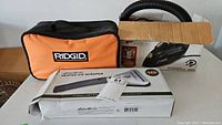 Lot items arranged: Ridgid carrying case, Dirt Devil vacuum in box, Eddie Bauer ice scraper box.