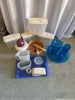 Overview of wooden salad bowl with serving spoons, white kitchen storage containers, blue pitcher set, and other plastic containers including onion holder.