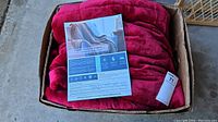 Red Sherpa weighted blanket folded inside a cardboard box with product information label visible.