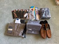Photo showing new pantyhose packages, men's pants, slippers, shoe liners, tablet case and pillow stand all laid out on carpeted floor.