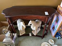 Front angle view showing dark wood table with curved edges, four legs, glass shelf, and decorative wooden horse sculptures underneath (not included).