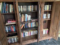 Wide shot of three wooden cabinet shelves filled with assorted paperback books mainly in genres of science fiction, crime, history, and novels.