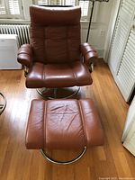 Front view of brown leather swivel chair and matching ottoman on hardwood floor