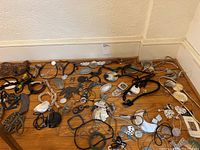 Wide view of assorted costume jewelry spread on wooden floor including necklaces with shells, beads, and metal pendants, bracelets and pins.