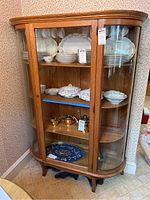Front view of oak cabinet filled with dishes showing curved glass door and rope trim