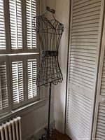 Overall view of the vintage wire dress form mannequin standing near a window and white louvered closet doors.