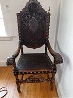 Front view of the chair showing embossed leather back and seat, brass studs and carved wood frame.