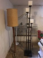 Pair of floor lamps side by side in a room, showing the natural cactus stem lamp with beige fabric shade and the taller modern metal lamp with glass shades.