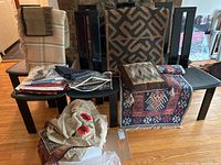 Wide shot showing multiple textiles including throw pillows, rugs, folded fabrics, and linens on chairs and floor.