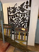 Wide view of the lot showing the metal Haitian bird wall art panel mounted on the wall with two wooden Indonesian panels leaning nearby, highlighting scale and condition.