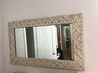 Full view of rectangular wall mirror hanging on wall showing geometric patterned wooden frame and clear reflective glass.