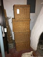 Four rectangular wicker baskets stacked, showing front and side metal handles, natural brown colour.