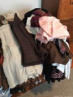 Overview of assorted women's clothing piled on a surface showing multiple colors and fabrics mostly in darker and neutral tones.