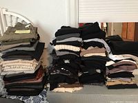 Full view of multiple stacks of folded women's designer clothing including shirts, tops and pants in neutral colors