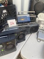 Photo showing black portable radios including two with HD Radio labels, a small white tabletop speaker radio, and a grey tabletop radio on a white table.