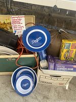 Photo shows a variety of camping accessories including a Coleman cooler, Dodgers plates, sleeping bag, extension cords, trash bags, and other packed camping items.