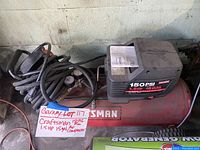 Full side view of Craftsman air compressor showing red tank, black motor housing, pressure gauges, and coiled air hose with attached plug and handle.