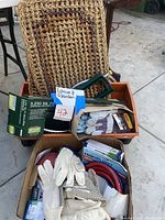 Photo showing boxes containing outdoor woven mats, garden gloves, a heavy duty red garden hose, a green metal fertilizer spreader, and oscillating sprinklers among other gardening tools and accessories.