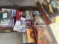 Overview photo of multiple boxed holiday greeting cards, some stacked and others in open boxes, with visible wrapping paper rolls to the right side.
