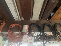 Photo showing 5 pairs of jumper cables and several extension cords coiled and hanging, with handwritten sign indicating jumper cables and heavy-duty extension cords.
