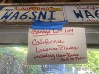 Photo showing multiple California license plates, including plates with ham radio call ID WA6SNI, taped sign with lot description in the background.