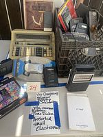 Various electronic devices including vintage calculator, Detectron Geiger counter, Monarch telegraph key, Sony voice recorder, and other small electronic items.