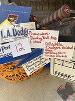 Photo showing assorted Dodgers memorabilia including Dodgers book, Dodgers World Champions magazine, handwritten note listing items, and vintage tennis racket handles.