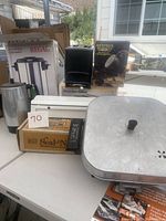 Top view photo showing Regal coffee maker box, Dormeyer fry pan with lid, microwave coffee brewer, Seal-a-Meal box and a metal pitcher on a table outdoor.