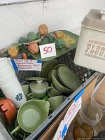 Photo showing avocado green melamine bowls, plates, pitchers, sugar bowl, and other kitchen items in a basket with a handwritten sign indicating 1970s melamine dishware.