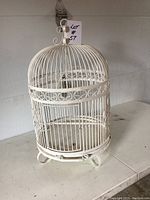 Full view of the white antique bird cage showing overall shape, top hook, and base feet.