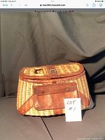 Front view showing woven wicker body, leather trim, and front pocket with flap secured by two rivets.