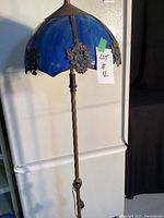 Full view of antique floor lamp showing twisted metal pole and blue slag glass shade with decorative metal accents.