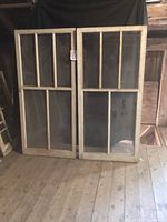 Two antique wooden windows leaning against a wall showing divided pane design and aged wood.