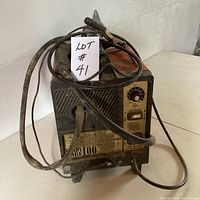 Front view of the ARC Weld 100 arc welder showing control panel, dial, label, power and electrode cables coiled on top.