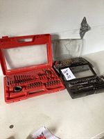 Photo showing two cases: red case with assorted drill and screwdriver bits, and black case with ratchet set and sockets.