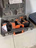 Open hard plastic case with Ridgid 18V cordless drill, impact driver, and battery charger inside, showing the tools and accessories included in lot.