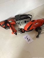Lot of three electric tools: an orange Black & Decker drill, a black Craftsman jigsaw, and an orange electric garden trimmer, all cords visible and placed on white tile floor.