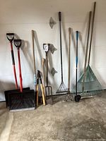 Full view of all garden tools against a garage wall showing shovels, rakes, pitchfork, hoe, and hand tool