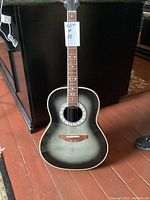 Full view of Ovation Celebrity CC64 guitar front showing includes black to gray sunburst finish, diamond-shaped inlays on fingerboard, and white-black decorative rosette around soundhole.