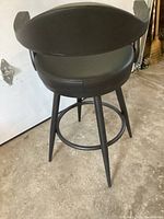 Overall view of the black leather bar stool with curved backrest and padded seat.