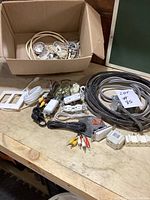 Box and various electrical items laid out on a wooden surface including cables, power strips, adapters, light fixtures, and switch covers