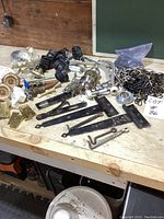 Overview of assorted metal hardware parts on wooden surface including hinges, door knobs, caster wheels, and chains.