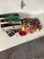 Overview of various tools including clamps, screwdrivers, small drill, and metal toolbox on a table