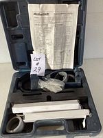 Mortising attachment components and instruction manual laid out in black molded plastic case, parts include blue plastic frame, white bars, plastic rings, and bagged pieces.