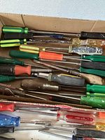 Full view of various screwdrivers laid out in cardboard box showing different handle colors and types.