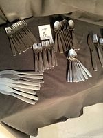 Overview of the stainless steel cutlery set spread on a black fabric background showing knives, forks, and spoons in groups.