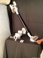 Full view of assembled vacuum with extension wand, brush head, additional attachments, charger and manual on black background