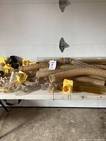 Overview of flexible corrugated vacuum hoses and various plastic fittings including yellow square base connectors and clear elbow pipes on a table against a garage door.